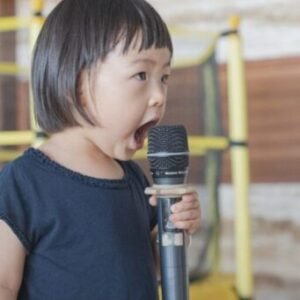 young girl in black blouse singing into microphone
