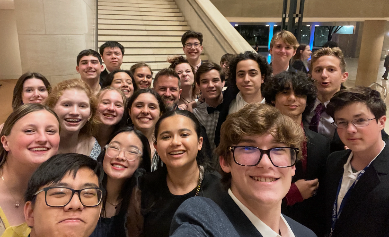 A large group of smiling teenage choir and musical theater students posing for a group photo inside a grand theater lobby