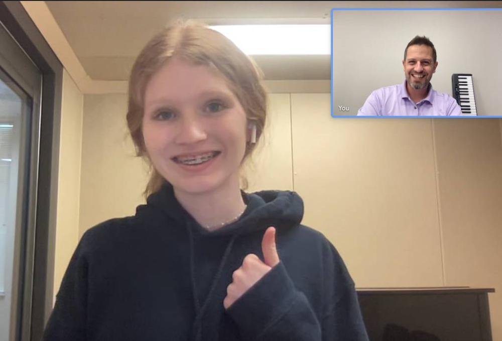 A split-screen view of a virtual music lesson with a smiling teenage girl giving a thumbs up and a male music instructor smiling from his studio in the corner window