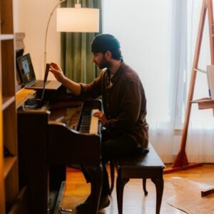 Man playing piano with laptop on stand.