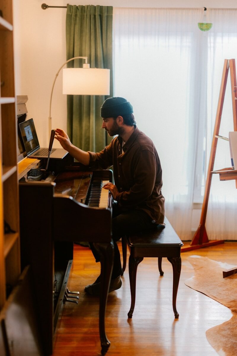 Man playing piano with laptop on stand.