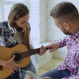 Man teaching woman to play guitar indoors